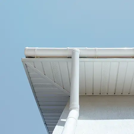 Weißes Fallrohr und Dachrinne an der Ecke eines Hauses vor blauem Himmel.